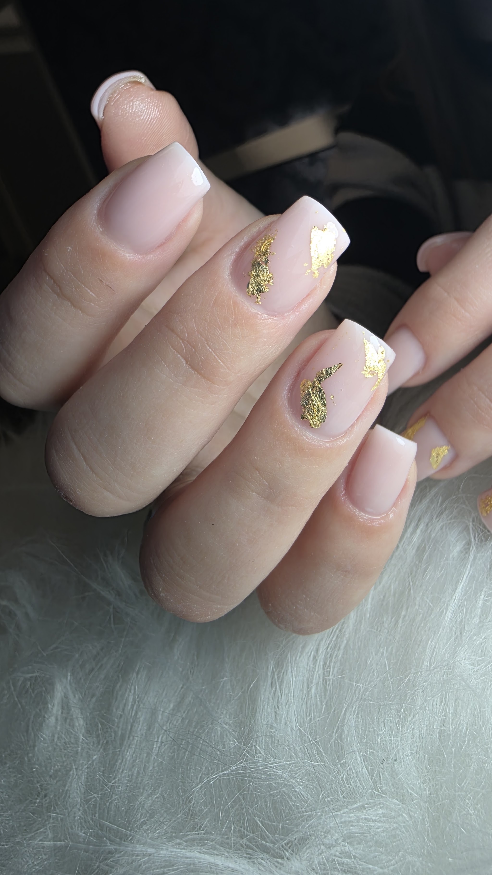 Naturel roze nagels met een witte French en stukjes bladgoud, op witte vacht