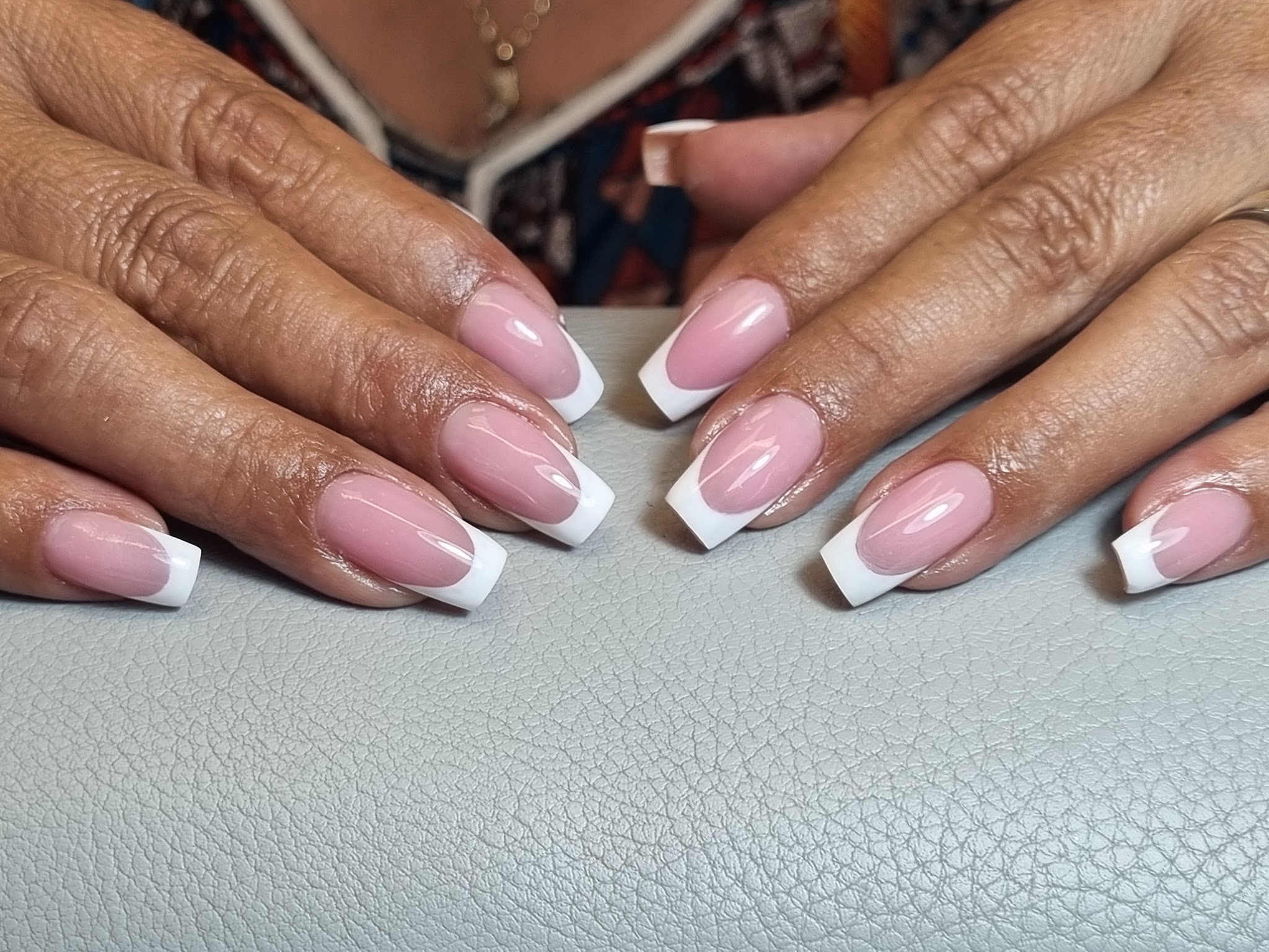 Twee handen met witte French op vierkante nagels, op de grijze armsteun