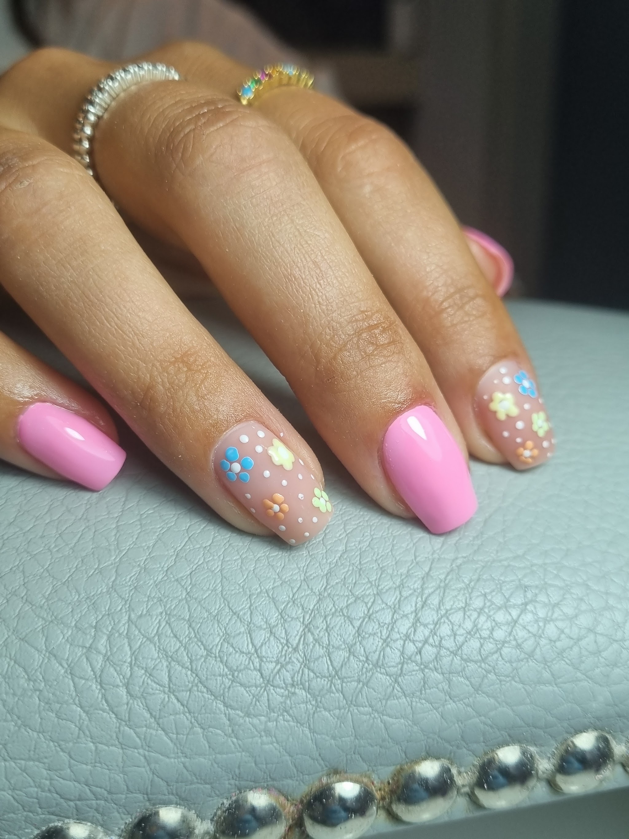 Roze nagels, twee ervan met bloemetjes, op de grijze armsteun