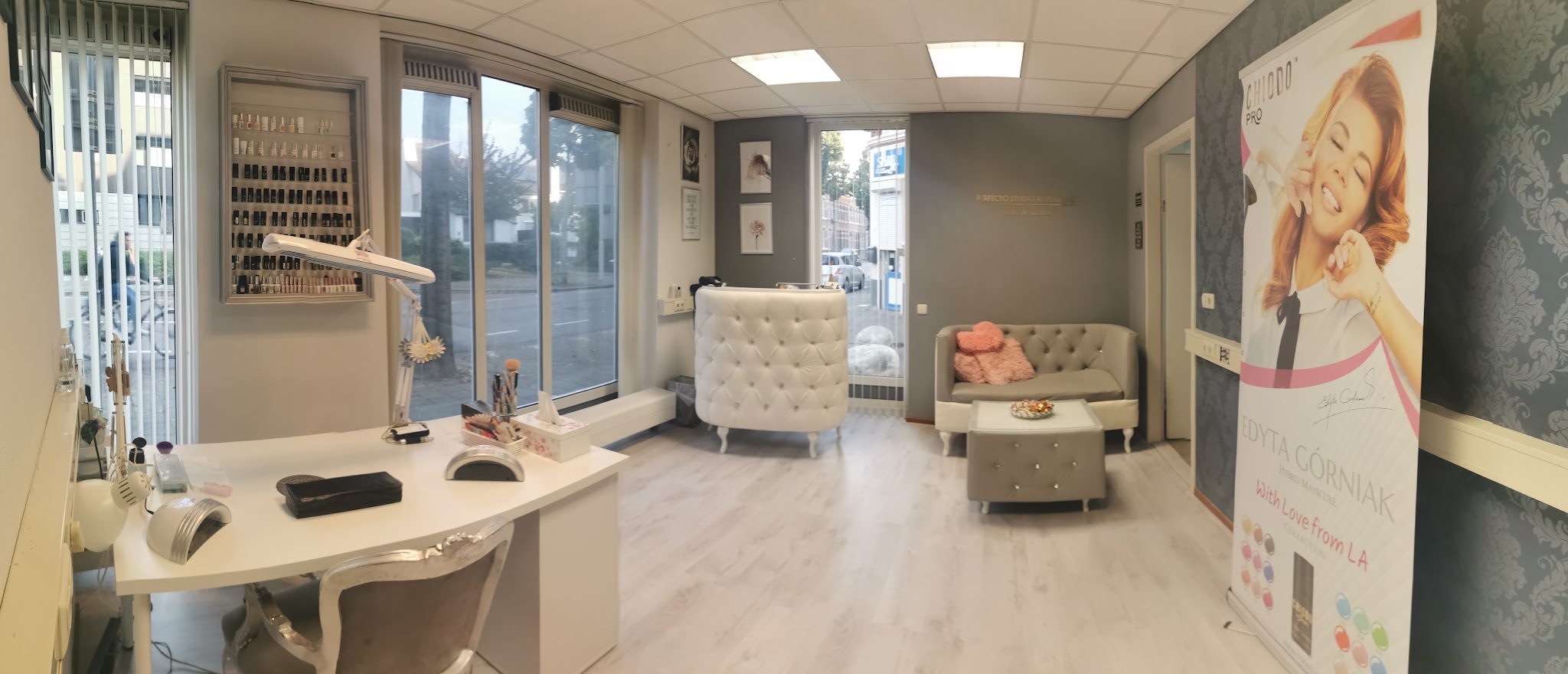 De studio: balie, behandelstoel, kleurenwand met nagellak en grote ramen aan de straatkant