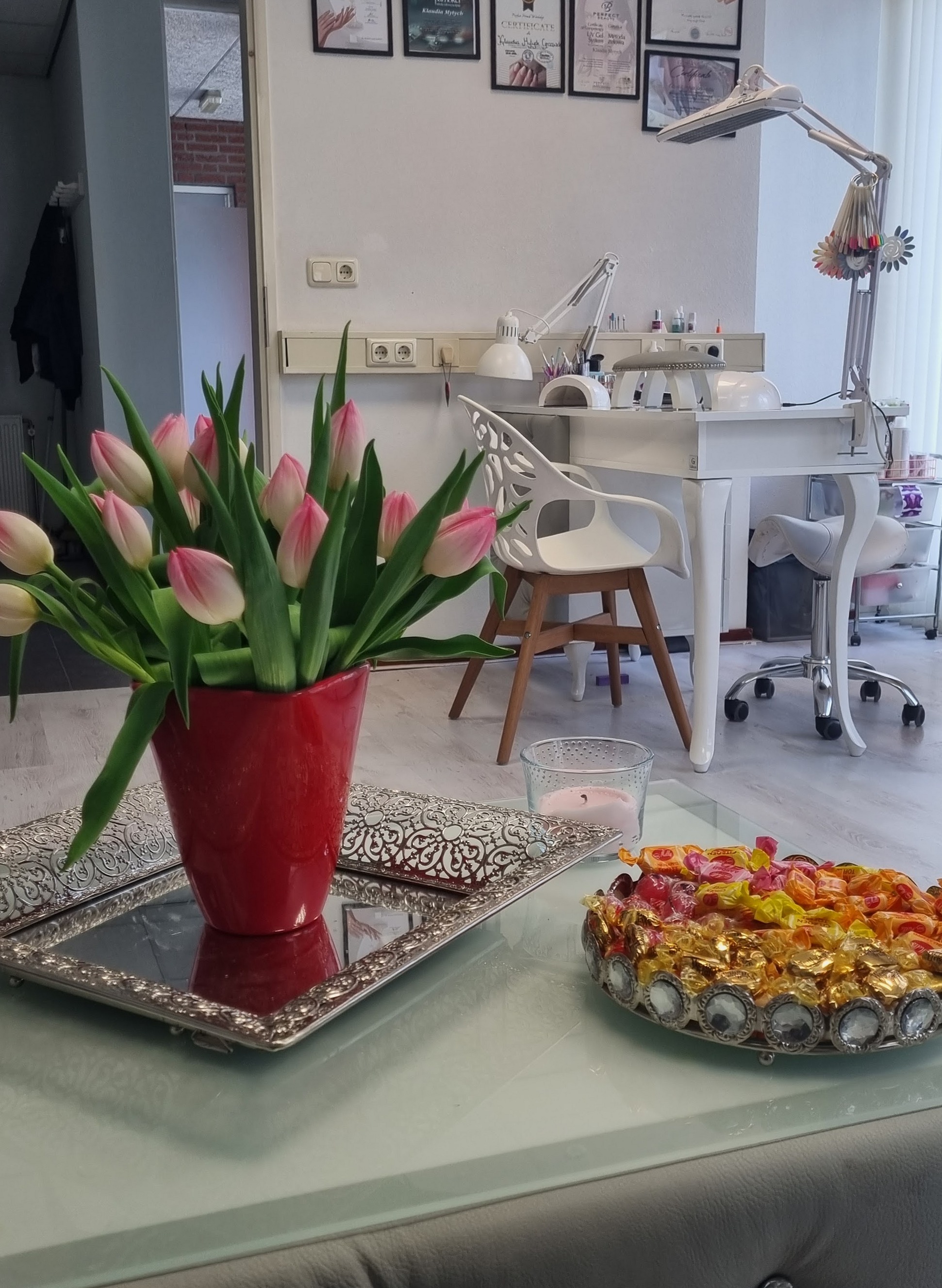 Roze tulpen in een rode vaas op een spiegelblad, met daarachter de behandeltafel van de studio