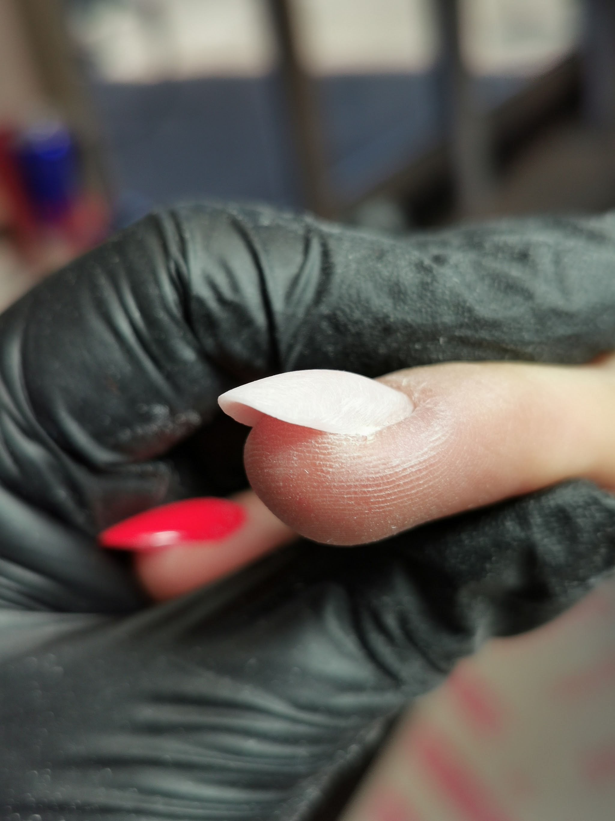 Een hand in een zwarte handschoen houdt een vinger vast met een nieuwe witte nageltip